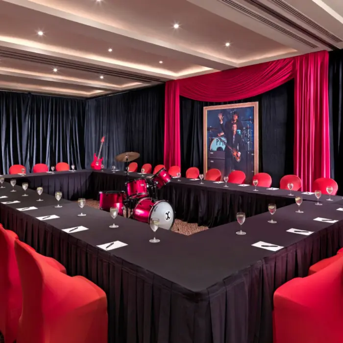 A U-shaped meeting room with black tablecloths, red chairs, and music-themed decor including a drum set.