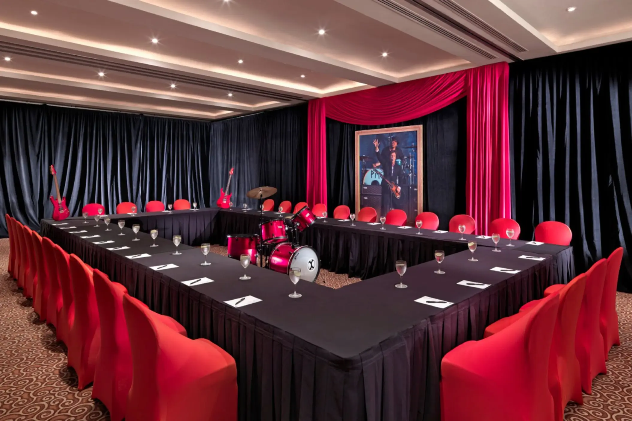 A U-shaped meeting room with black tablecloths, red chairs, and music-themed decor including a drum set.