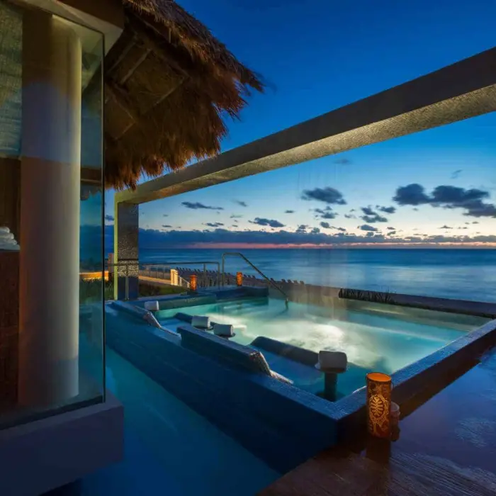 A serene spa hydro-jet pool with a thatched roof, overlooking the ocean at sunset.