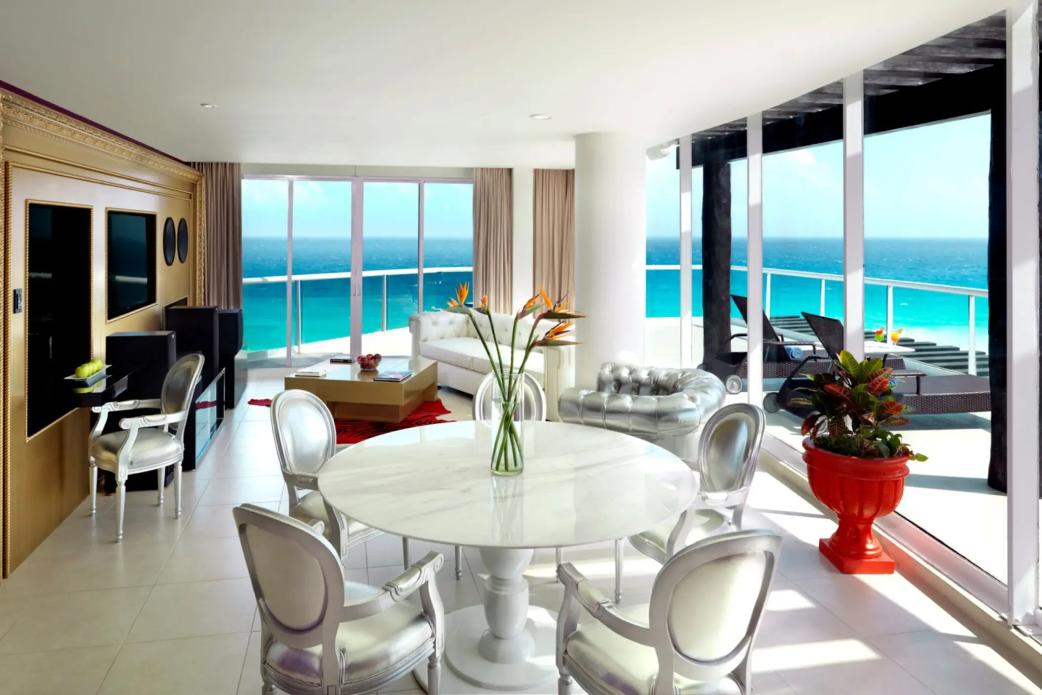 A luxurious suite living area with a dining table and floor-to-ceiling windows overlooking the ocean.