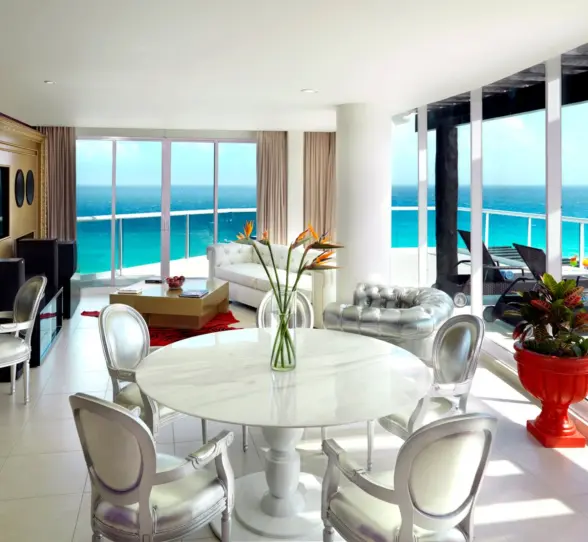A luxurious suite living area with a dining table and floor-to-ceiling windows overlooking the ocean.