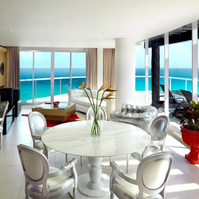 A luxurious suite living area with a dining table and floor-to-ceiling windows overlooking the ocean.