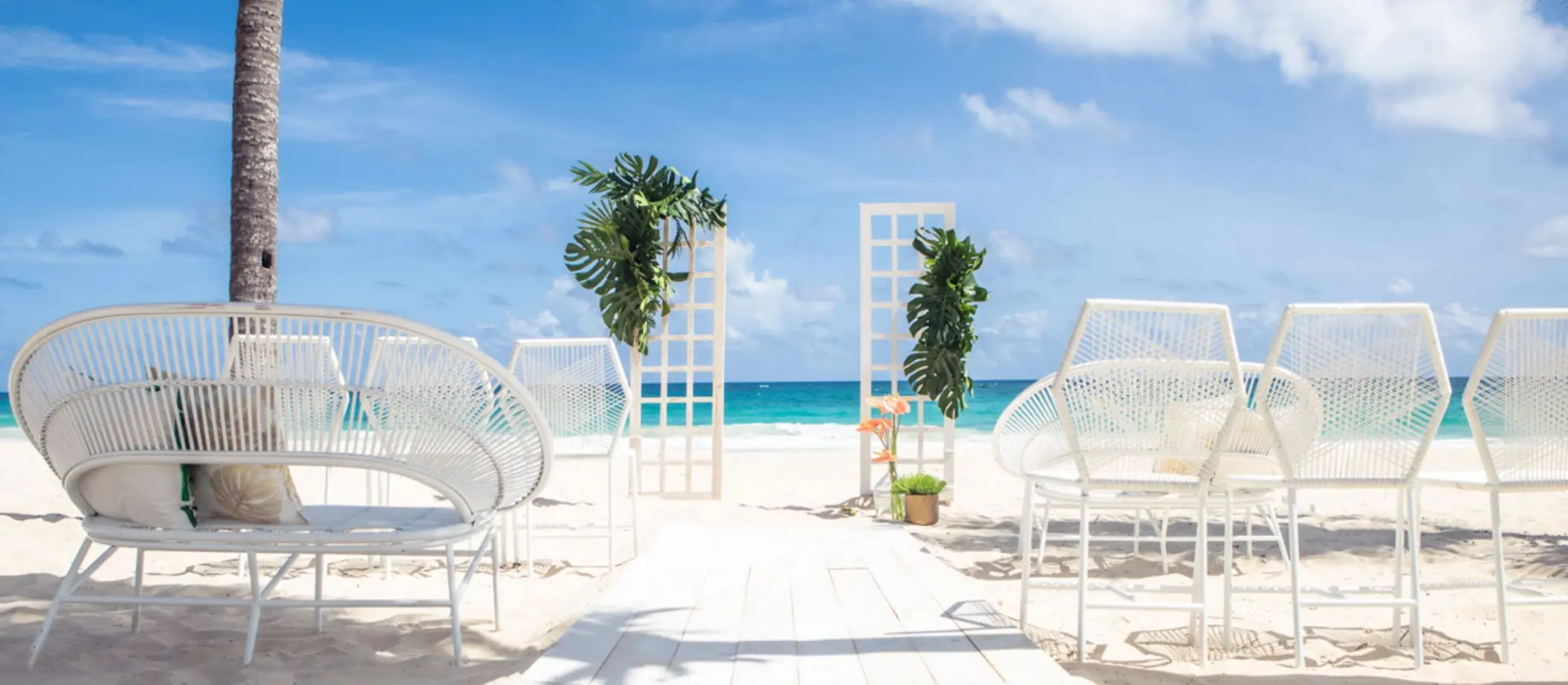 A beautiful beach wedding setup with white chairs, a decorative arch, and a pathway leading to the water.