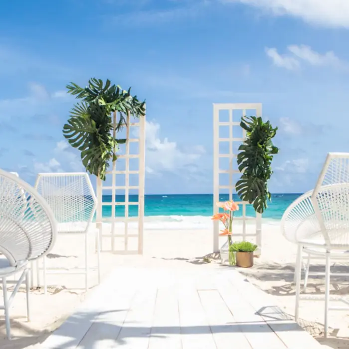 A beautiful beach wedding setup with white chairs, a decorative arch, and a pathway leading to the water.