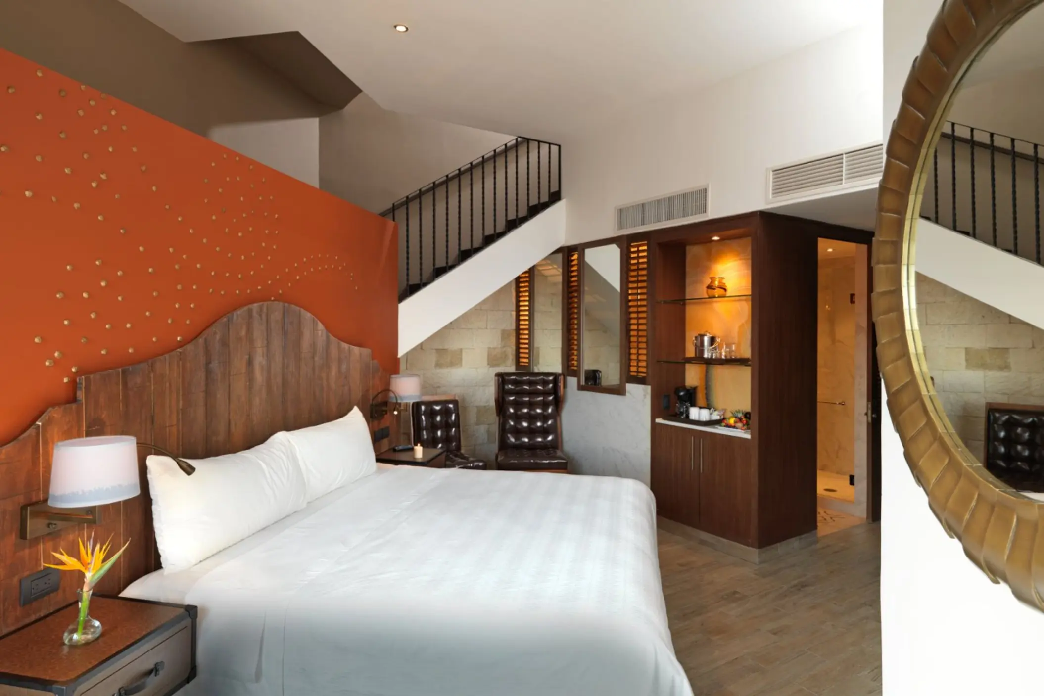A bright, two-story suite with a wooden headboard, staircase, and a large mirror in the corner.