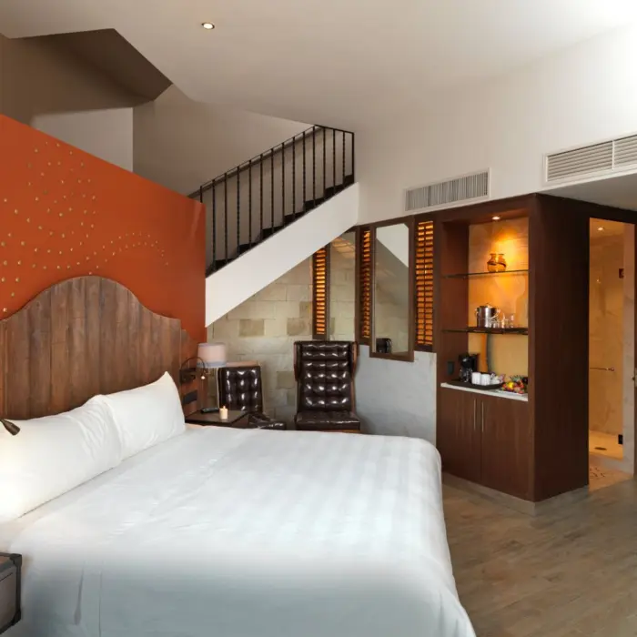 A bright, two-story suite with a wooden headboard, staircase, and a large mirror in the corner.