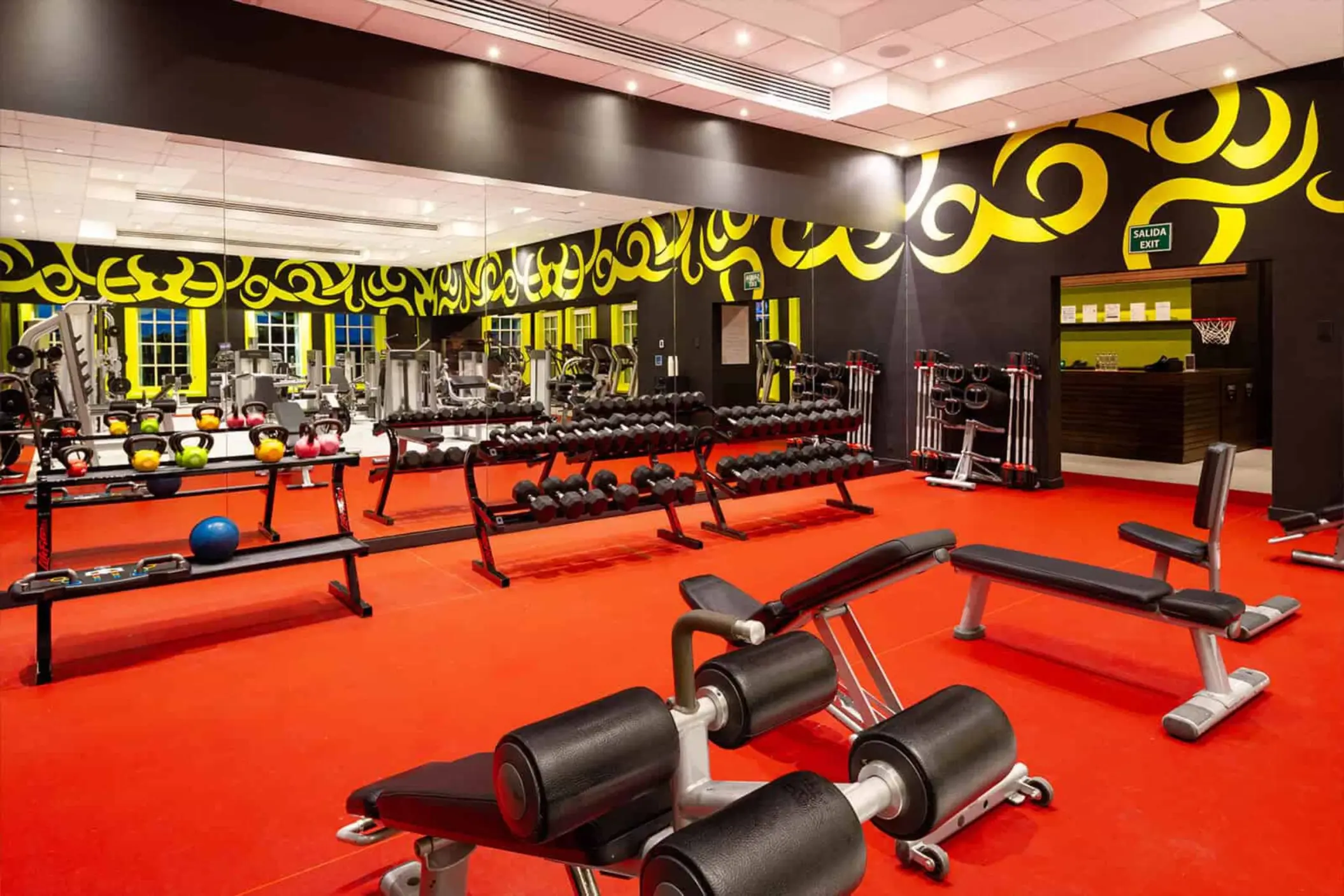 A vibrant and well-equipped gym with red flooring, various weights, and cardio machines.