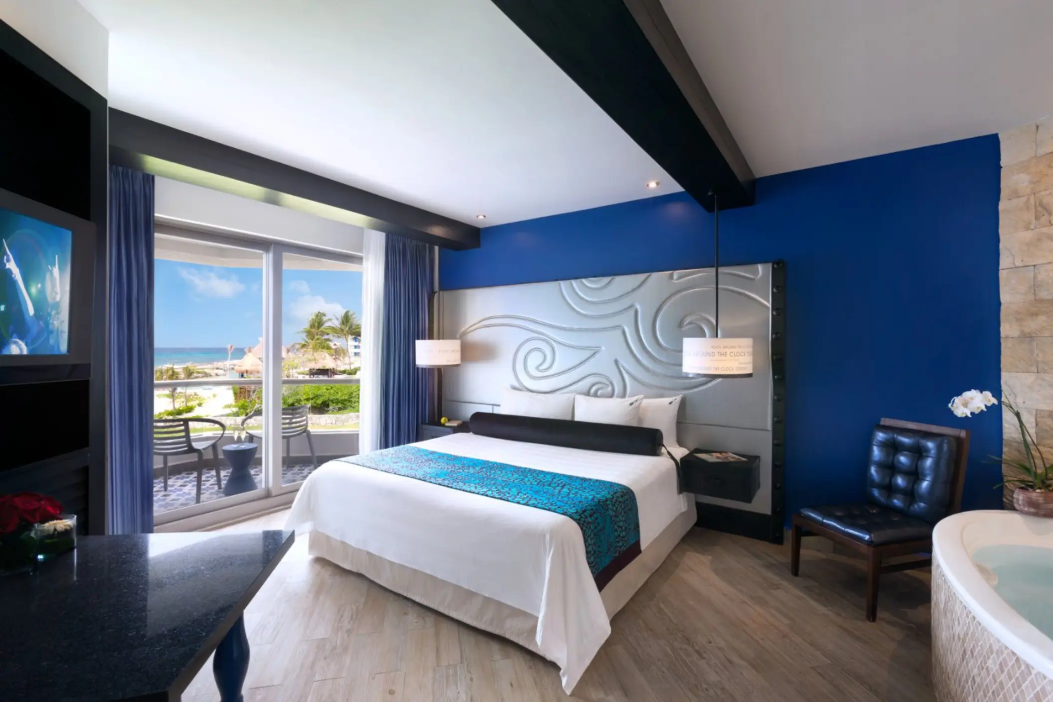 A stylish hotel room with a king-sized bed, a private balcony, and a whirlpool tub in the corner.