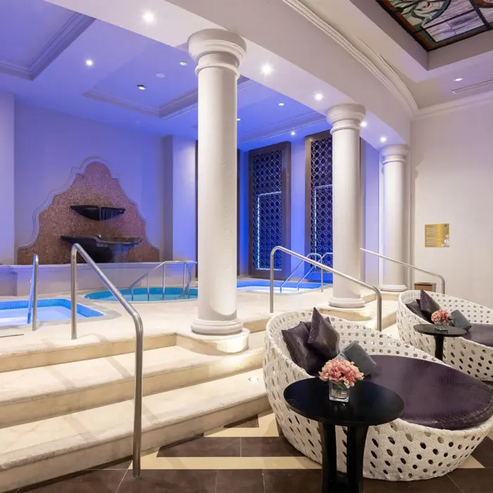 Two white loungers sit next to a relaxing indoor jacuzzi with elegant pillars at the Rock Spa.