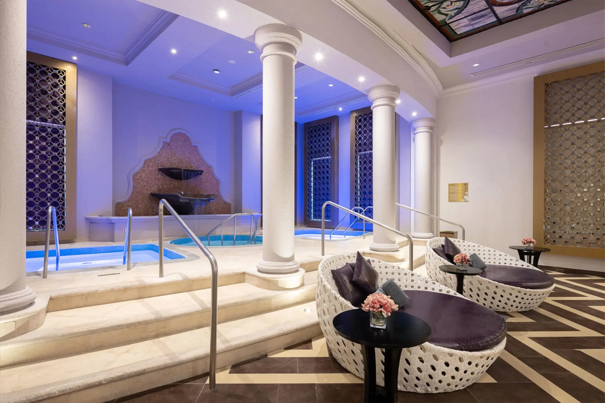 Two white loungers sit next to a relaxing indoor jacuzzi with elegant pillars at the Rock Spa.
