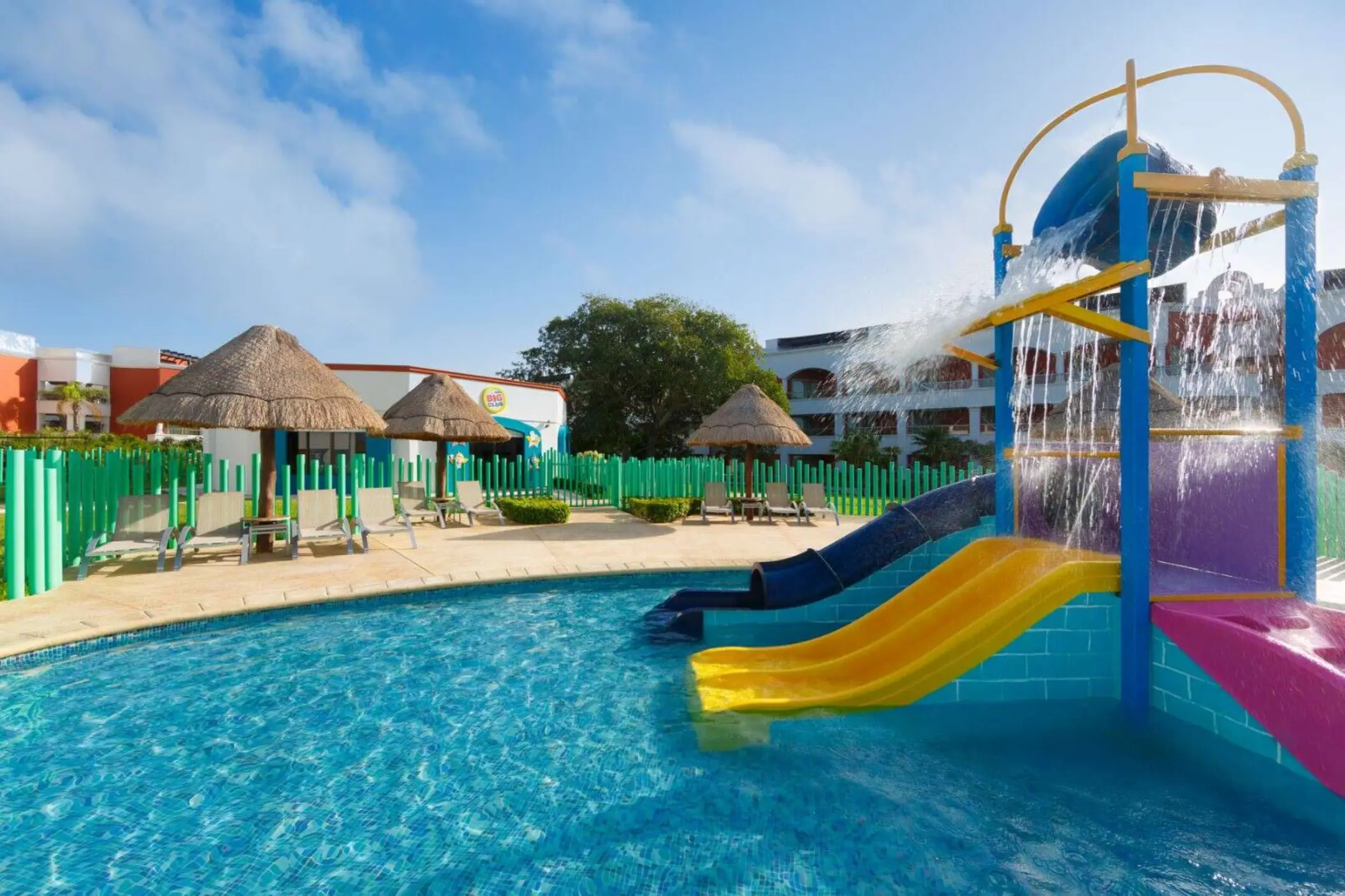 A shallow children's pool with colorful water slides and bright green fences.