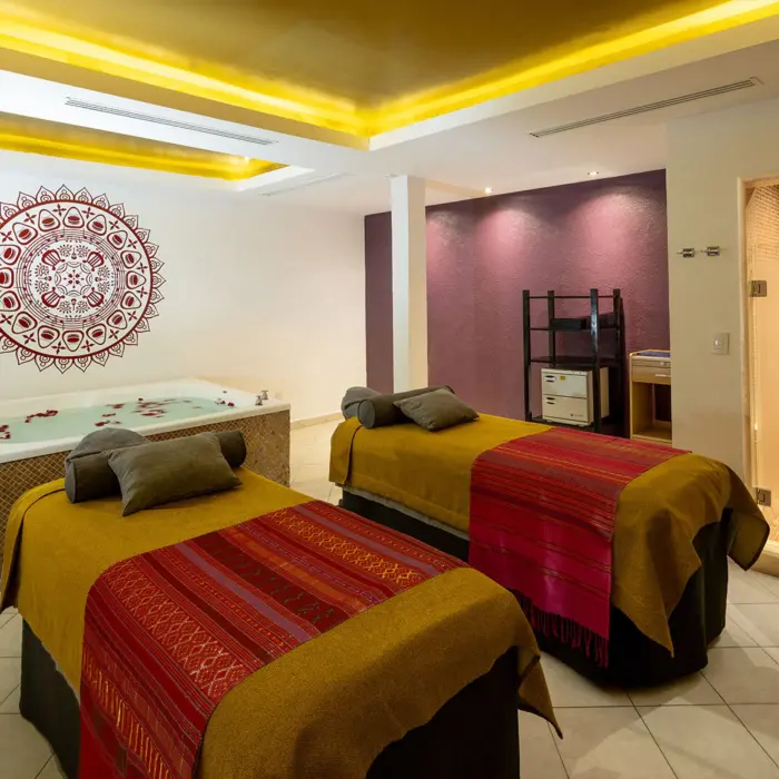 A luxurious spa room with two massage beds and a whirlpool tub filled with flower petals.