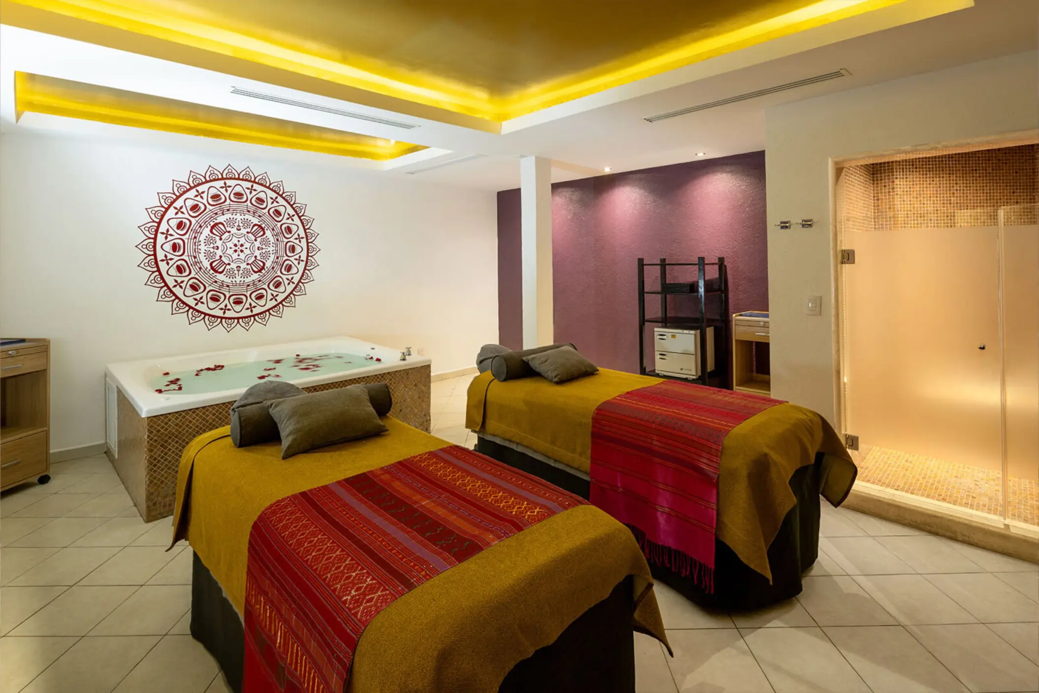 A luxurious spa room with two massage beds and a whirlpool tub filled with flower petals.