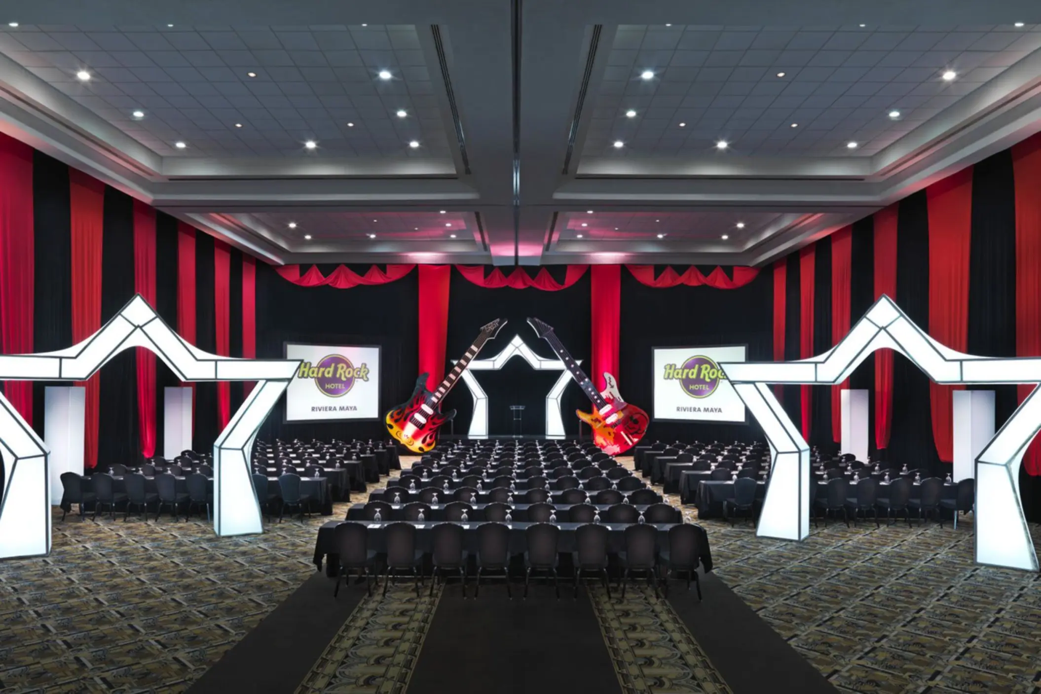A large, dark conference room with rows of chairs and two large guitars decorating the stage.