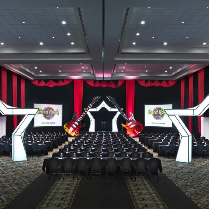 A large, dark conference room with rows of chairs and two large guitars decorating the stage.