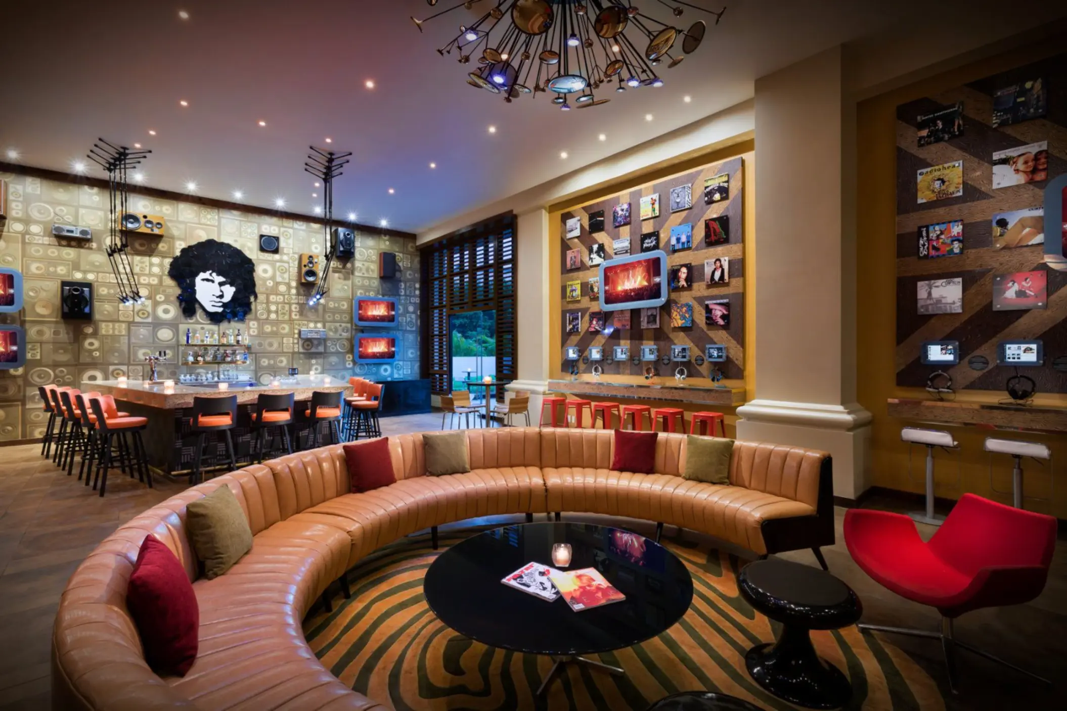 An eclectic bar with a curved sofa, a large mural, and record album art on the walls.