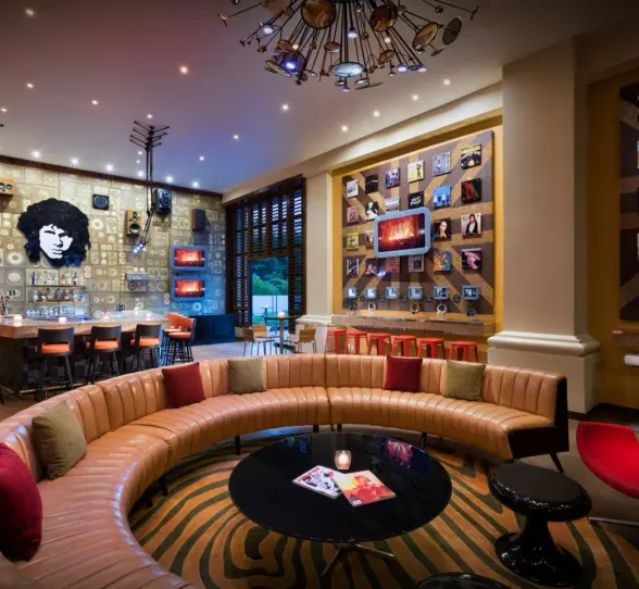 An eclectic bar with a curved sofa, a large mural, and record album art on the walls.
