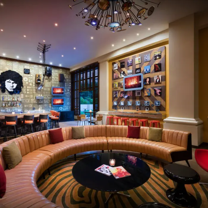 An eclectic bar with a curved sofa, a large mural, and record album art on the walls.
