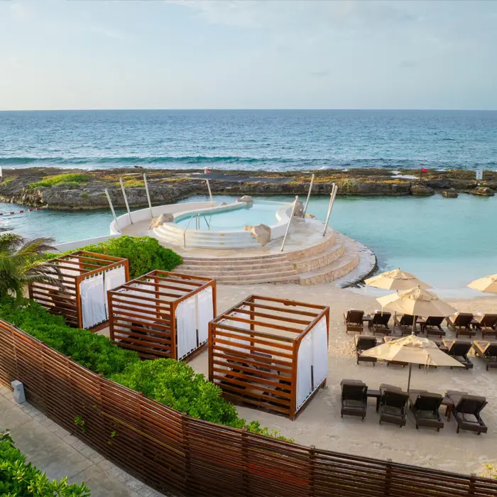 An elevated view of a protected cove beach with lounge chairs, cabanas, and a circular pool.