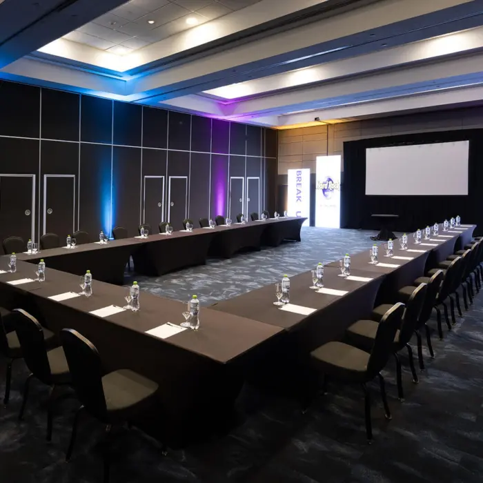 A modern U-shaped conference room with a large projector screen and purple and blue lighting.