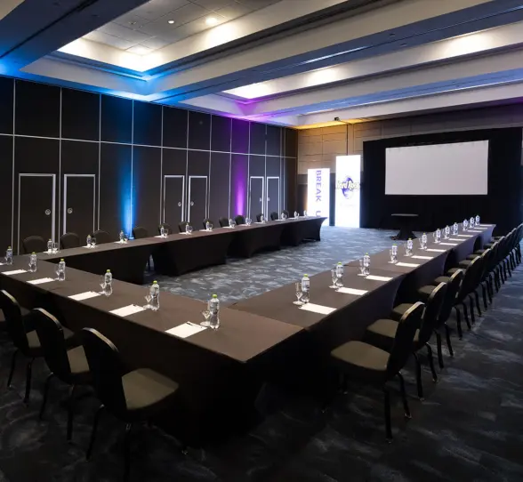 A modern U-shaped conference room with a large projector screen and purple and blue lighting.