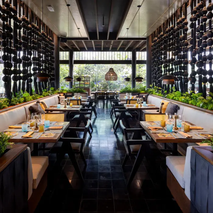 An elegant, symmetrical restaurant with booth seating, plants, and a unique hanging art installation.