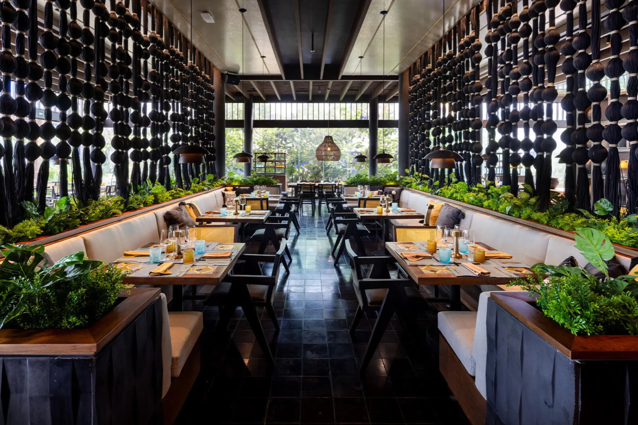 An elegant, symmetrical restaurant with booth seating, plants, and a unique hanging art installation.