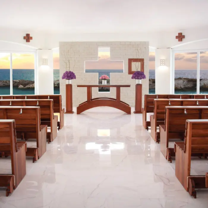 A beautiful indoor wedding chapel with rows of wooden benches and large windows overlooking the ocean.