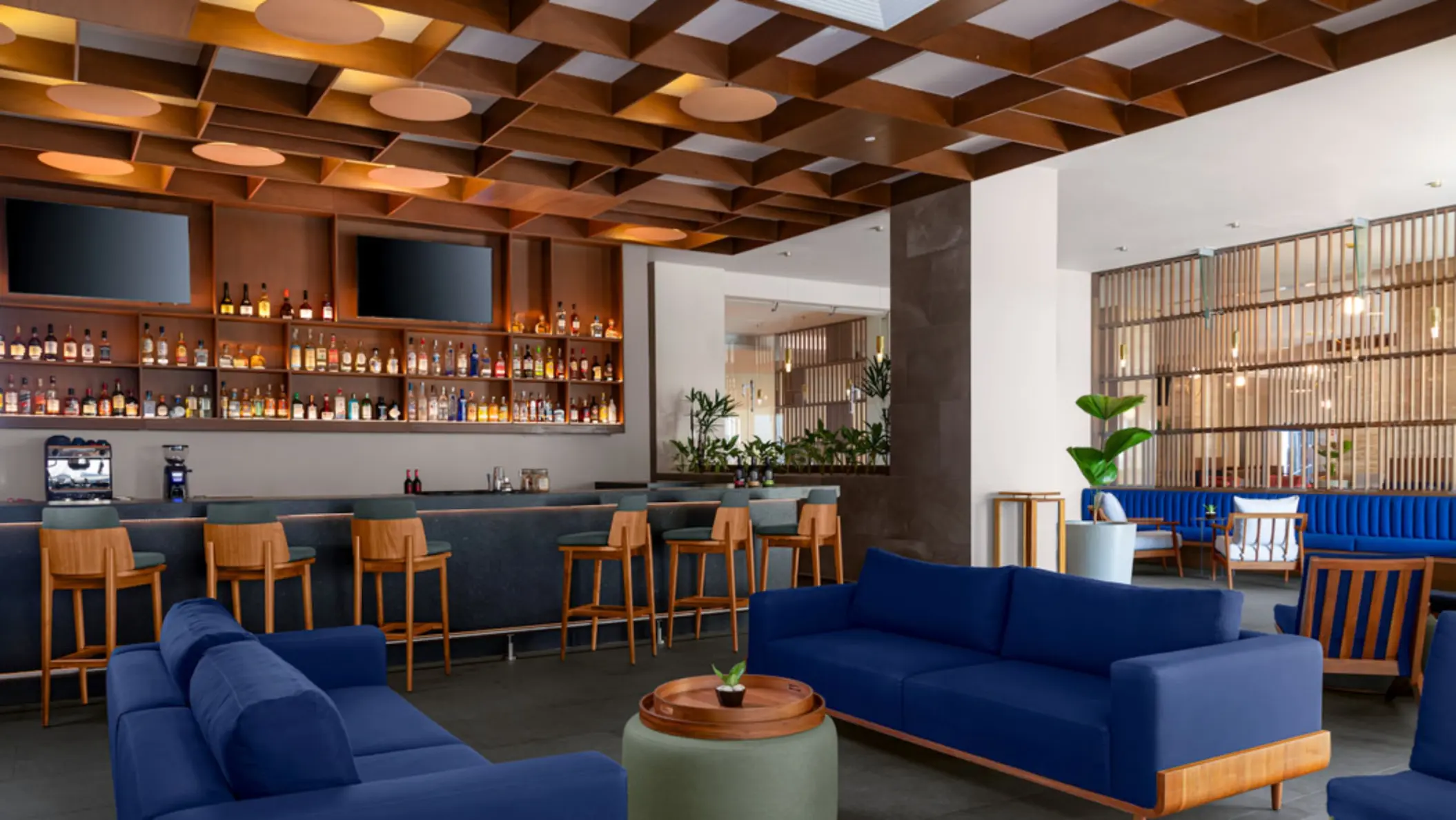 An upscale bar area with a fully stocked liquor shelf, dark bar counter, and comfortable blue sofas in a lounge setting.