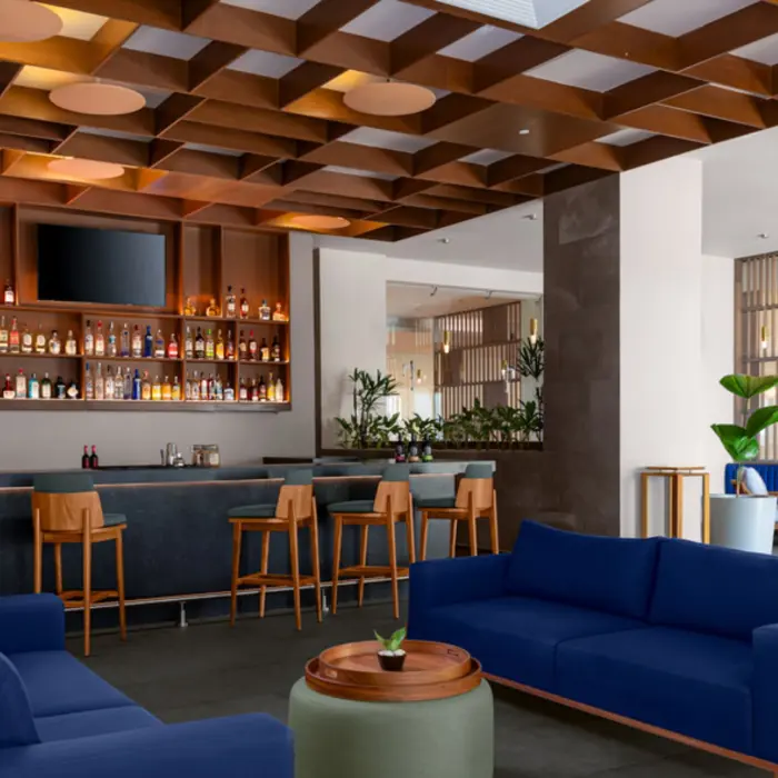 An upscale bar area with a fully stocked liquor shelf, dark bar counter, and comfortable blue sofas in a lounge setting.