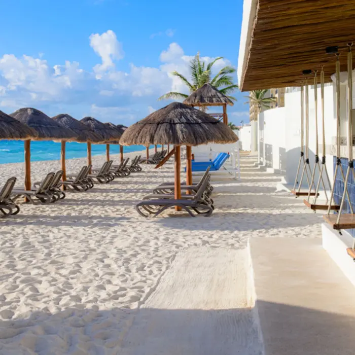 A relaxing beach bar with thatched-roof umbrellas, lounge chairs on white sand, and swing seats at the bar counter.