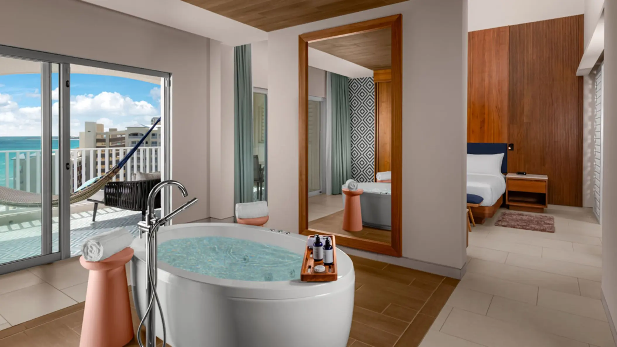 An elegant hotel suite with a large freestanding bathtub, a hammock on a balcony, and a comfortable bed in the background.