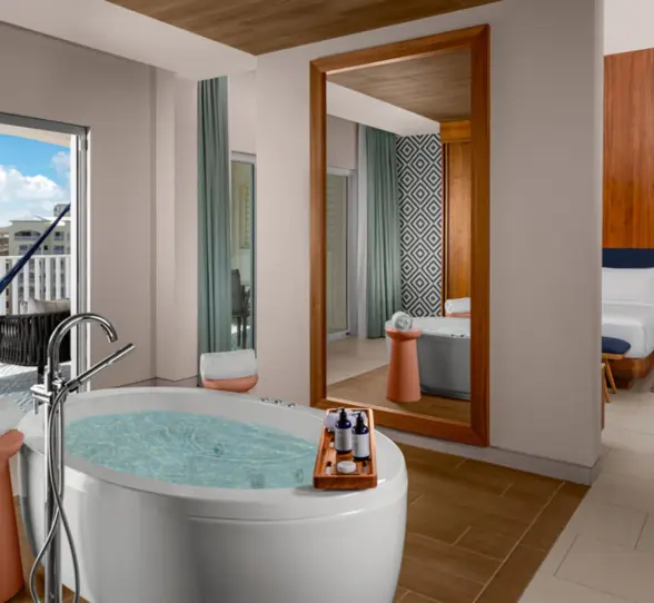 An elegant hotel suite with a large freestanding bathtub, a hammock on a balcony, and a comfortable bed in the background.