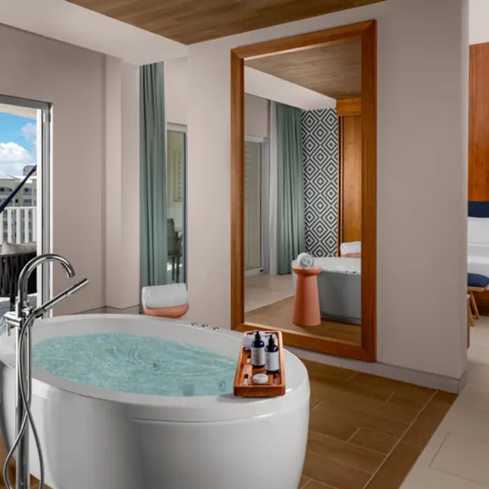 An elegant hotel suite with a large freestanding bathtub, a hammock on a balcony, and a comfortable bed in the background.