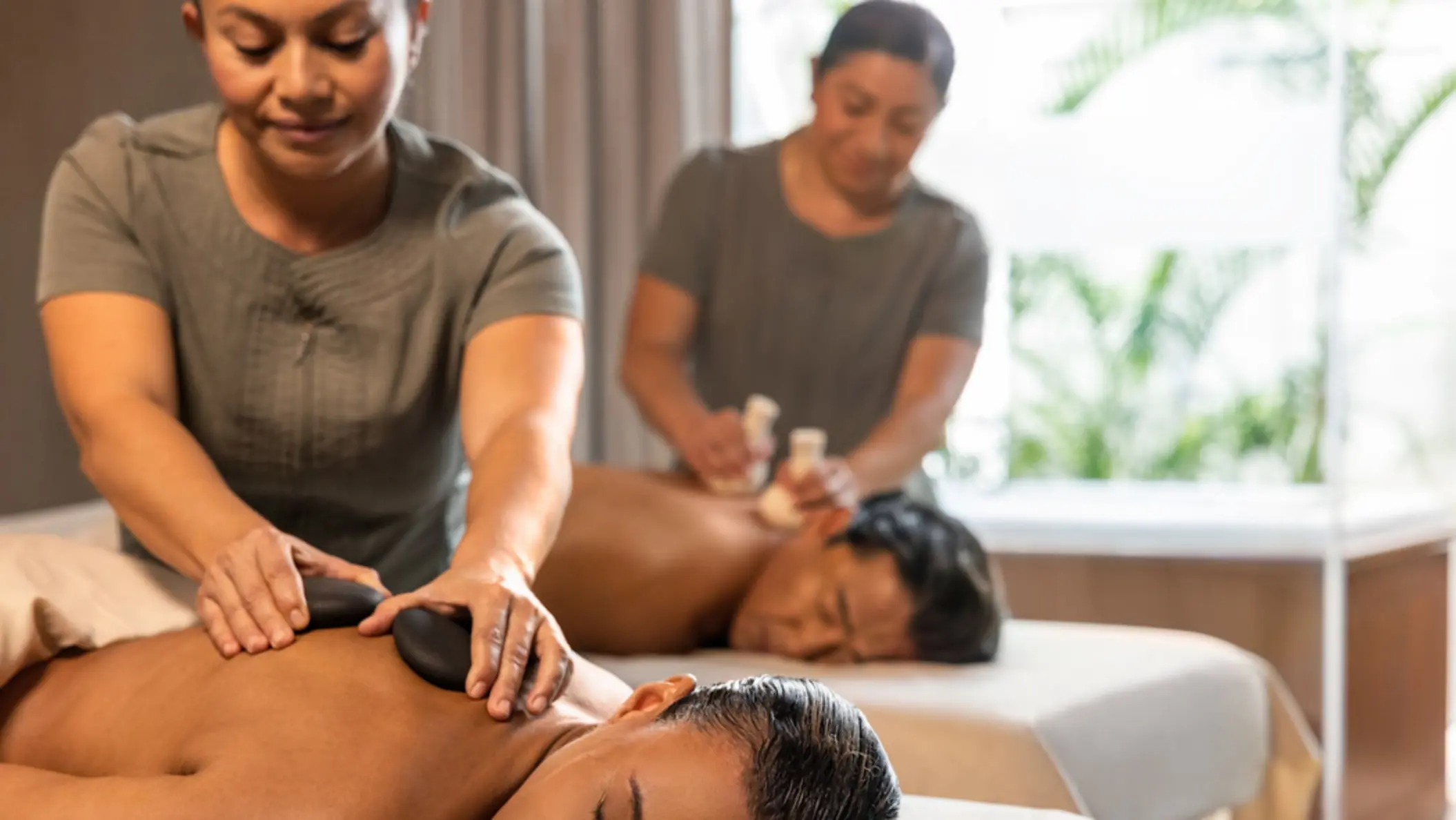 Two people receiving relaxing massages at a spa, one with hot stones and another with herbal pouches.