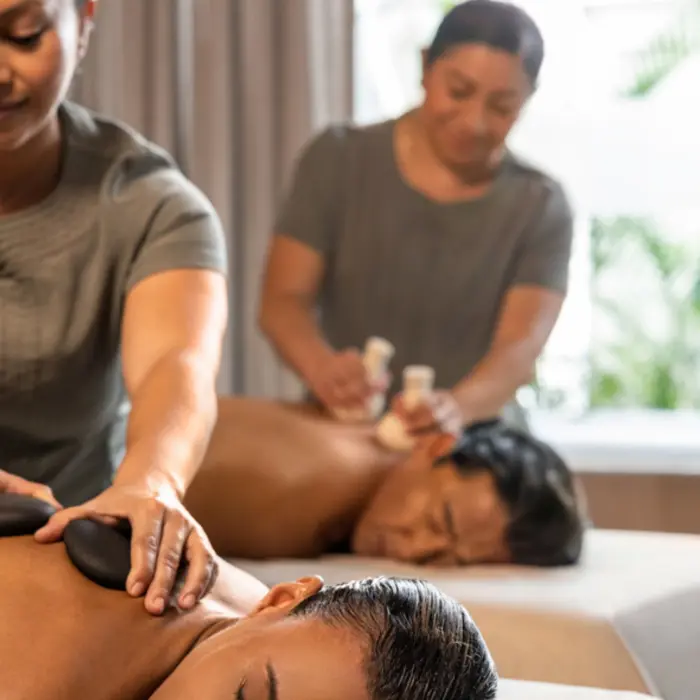Two people receiving relaxing massages at a spa, one with hot stones and another with herbal pouches.