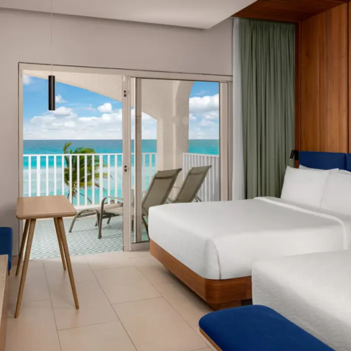 A hotel suite with two double beds, a television, and a balcony with an incredible ocean view.