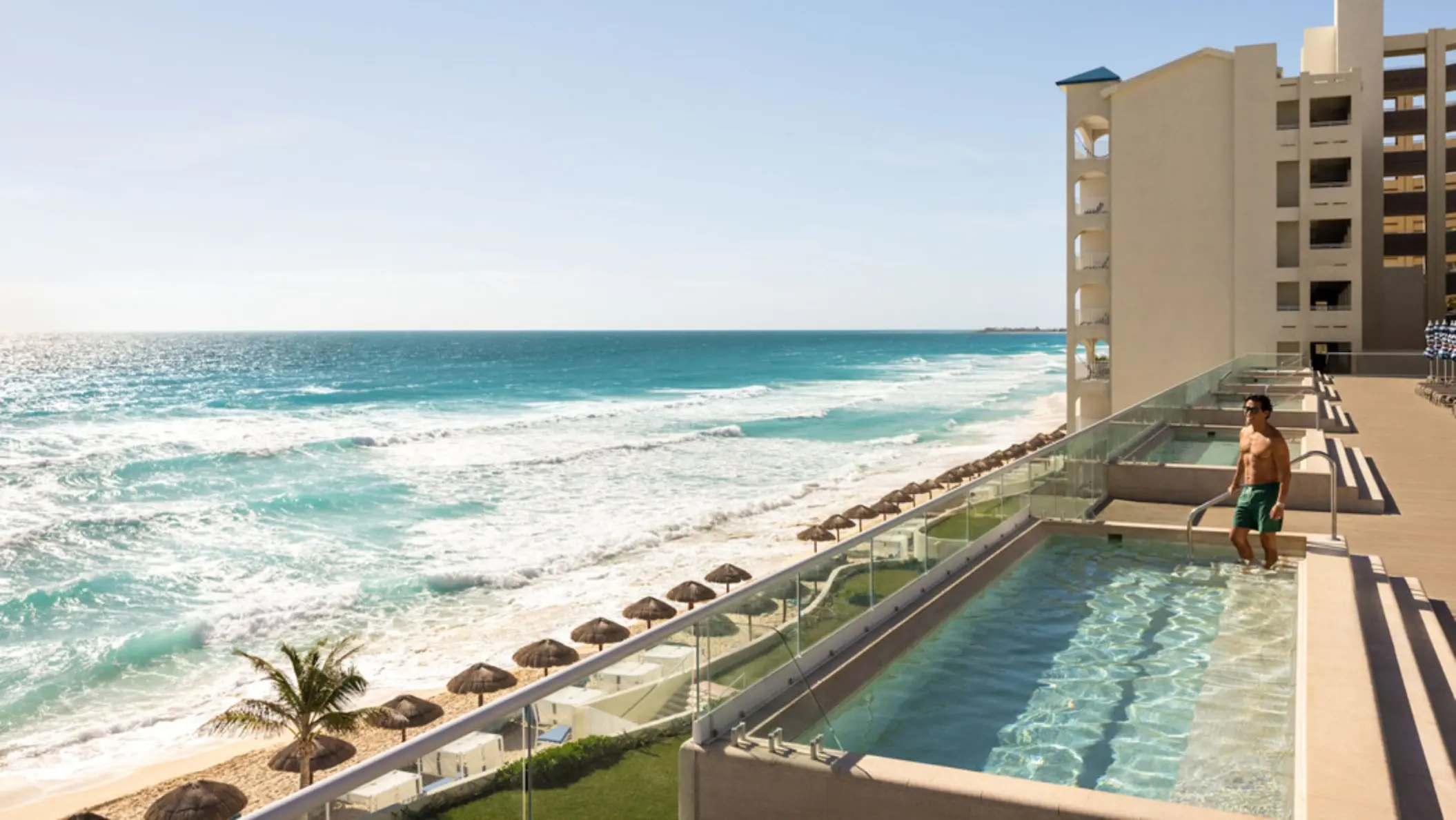 A man standing in a rooftop plunge pool overlooking a sundeck and the stunning ocean waves.