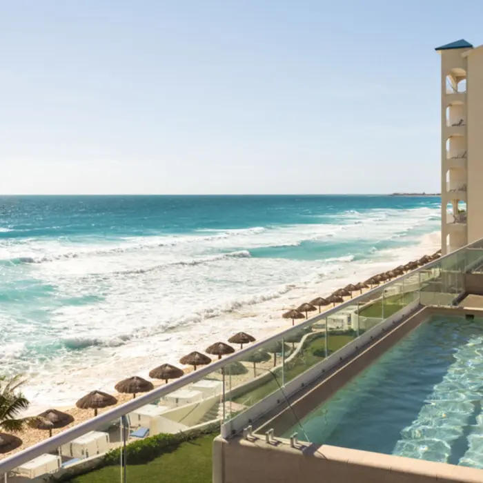 A man standing in a rooftop plunge pool overlooking a sundeck and the stunning ocean waves.