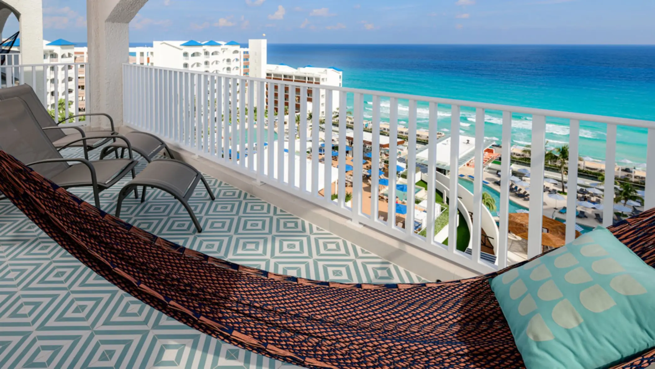 A beautiful balcony with a patterned floor, hammock, lounge chairs, and an expansive view of the ocean.