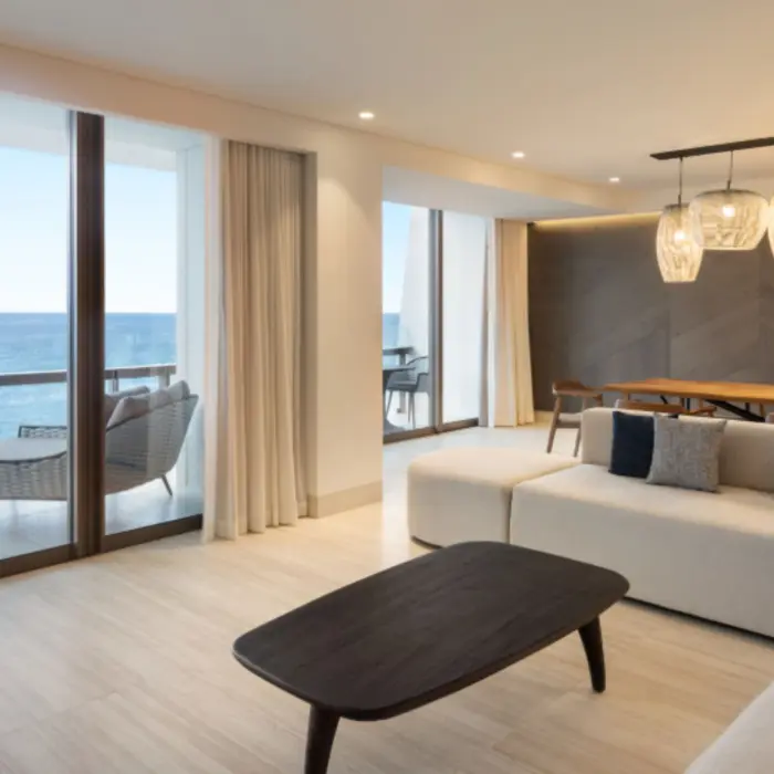 Oceanview suite with modern living area, large sectional, wooden dining table, and access to a private balcony.