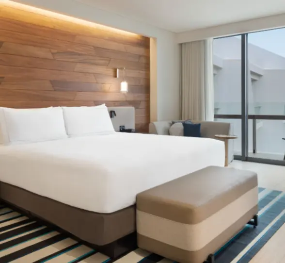 Contemporary guest room with king bed, wood-paneled headboard, cozy sitting area, and floor-to-ceiling windows.