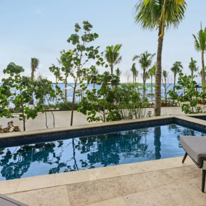 Private swim-up suite patio with woven chairs, stone deck, and small pool framed by tropical plants and palm trees.