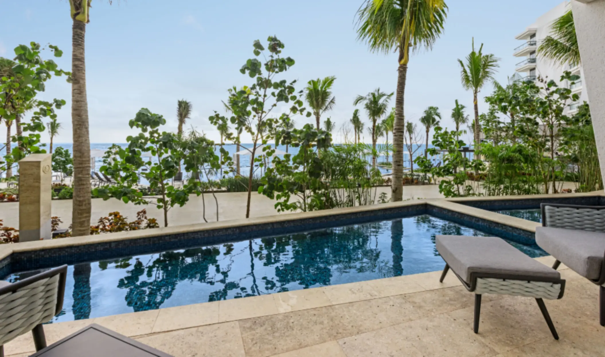 Private swim-up suite patio with woven chairs, stone deck, and small pool framed by tropical plants and palm trees.