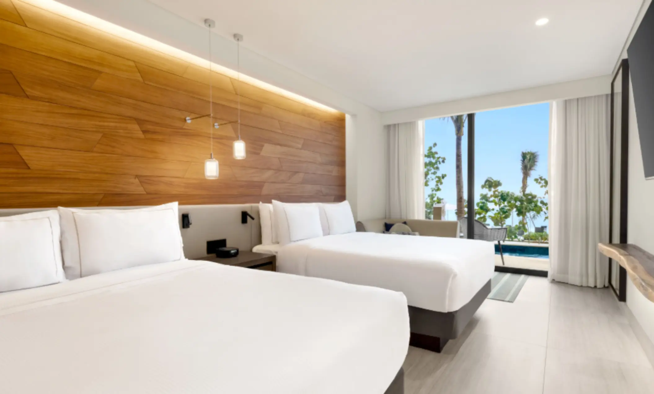 Bright room with two queen beds, wooden headboard, and a view of the plunge pool and lush greenery outside.
