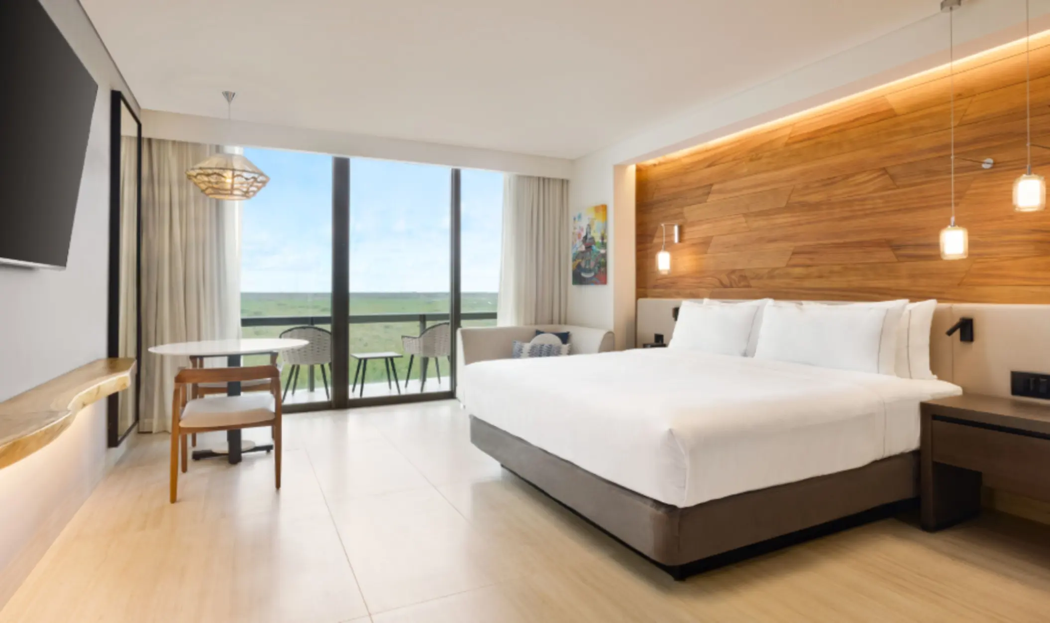 Stylish guest room with king bed, light wood floors, and private balcony overlooking tropical landscape.