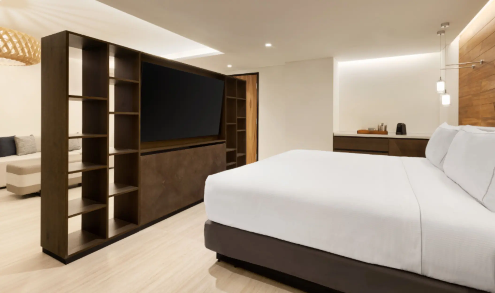Spacious suite with king bed, large TV on open shelving, and modern layout with clean lines and soft lighting.
