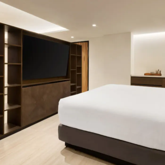 Spacious suite with king bed, large TV on open shelving, and modern layout with clean lines and soft lighting.