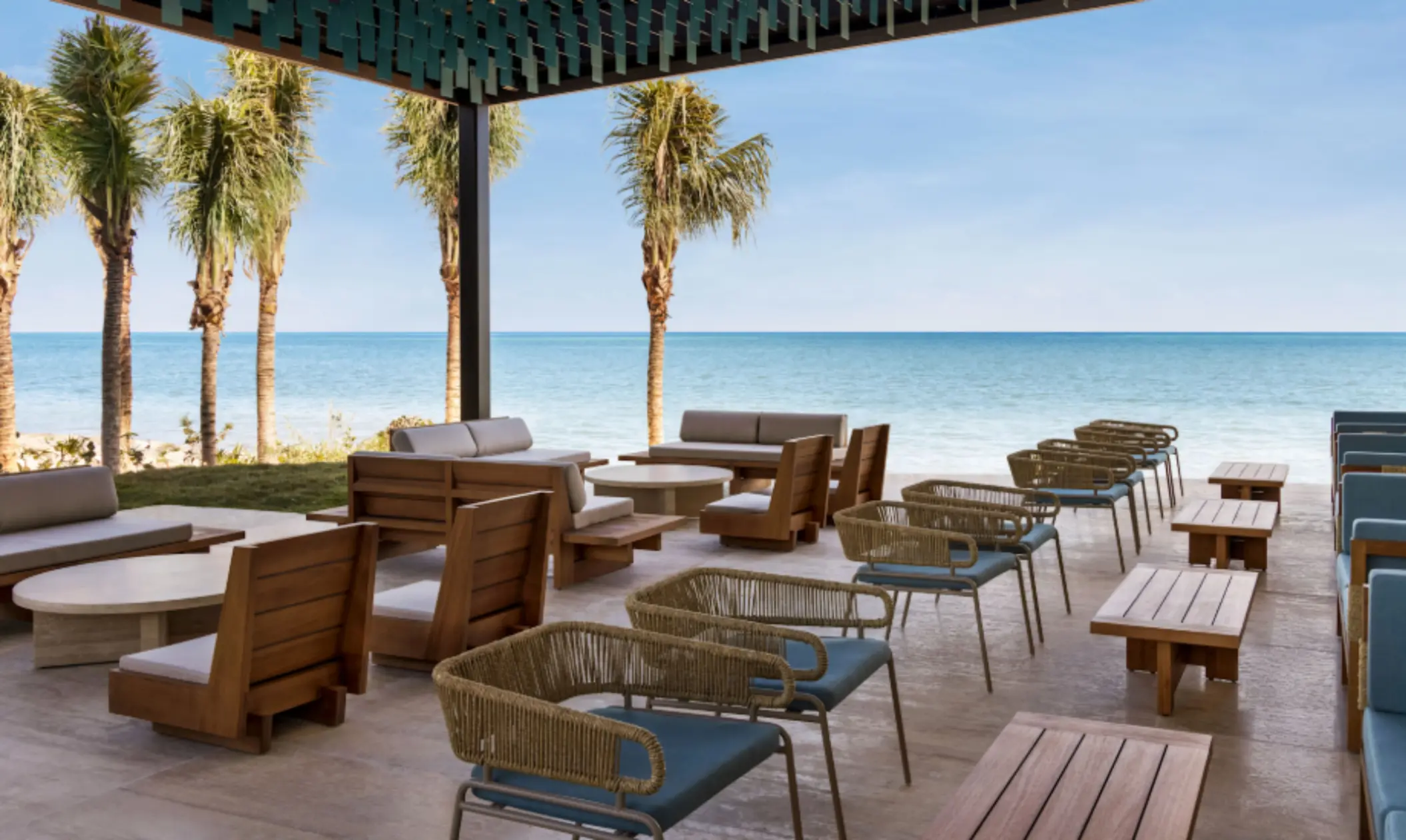 Outdoor lounge with oceanfront views, wooden furniture, and palm trees offering a relaxing beachfront seating experience.