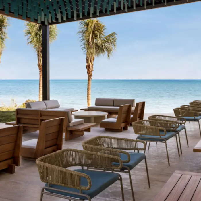 Outdoor lounge with oceanfront views, wooden furniture, and palm trees offering a relaxing beachfront seating experience.